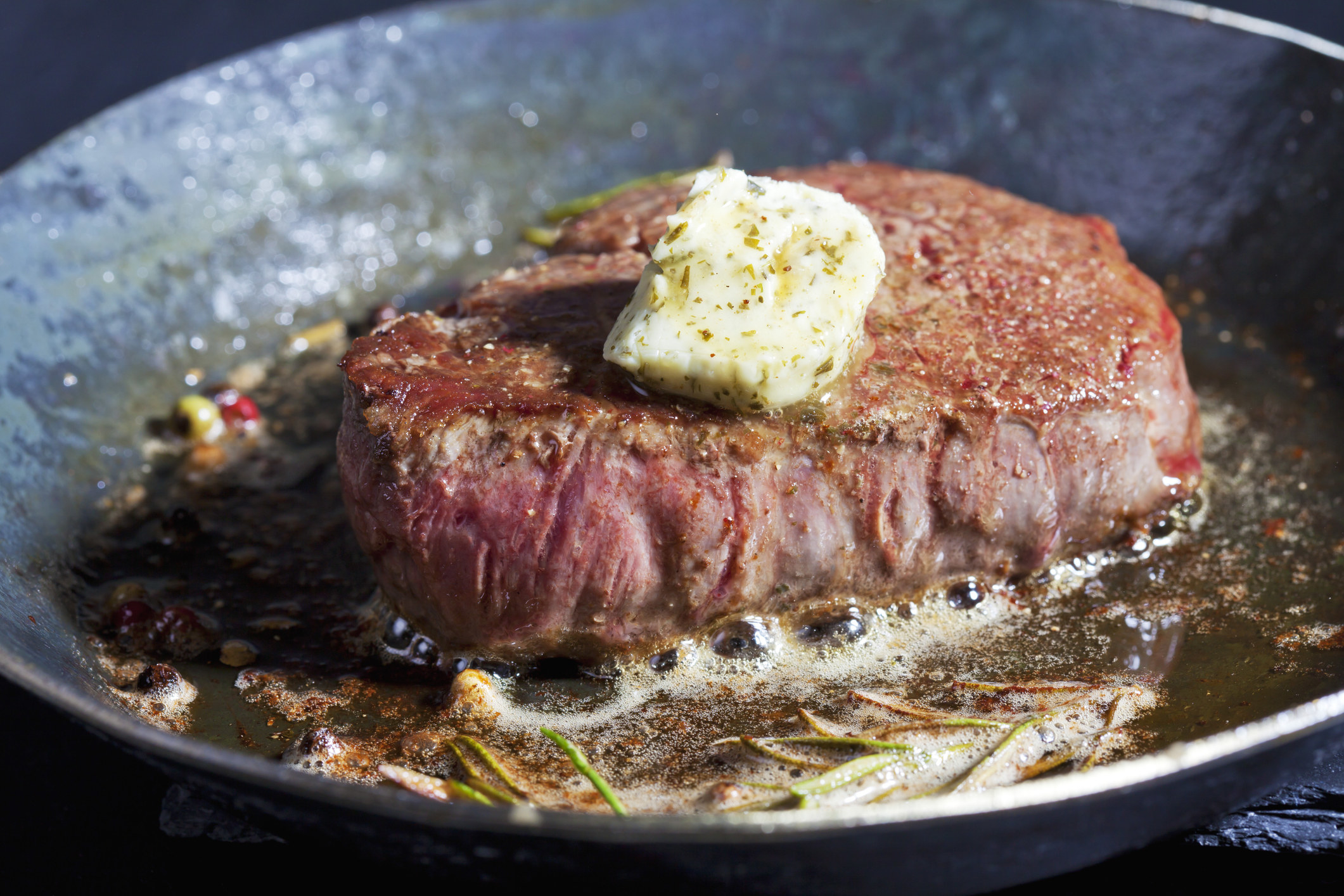 A fillet of beef with herb butter, peppercorns and rosemary in a pan.