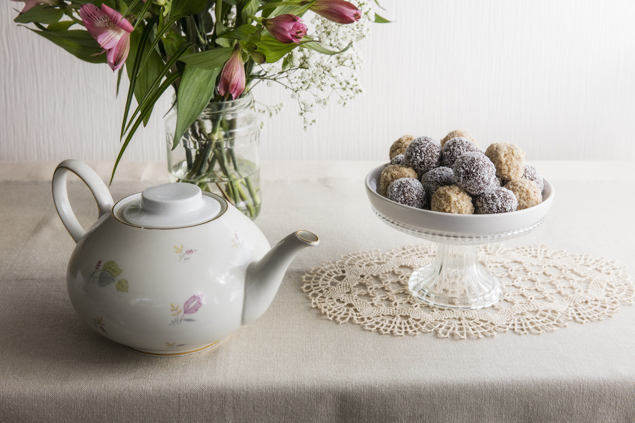 A teacup, vase with flowers, and truffle chocolates in a platter with a doily below it