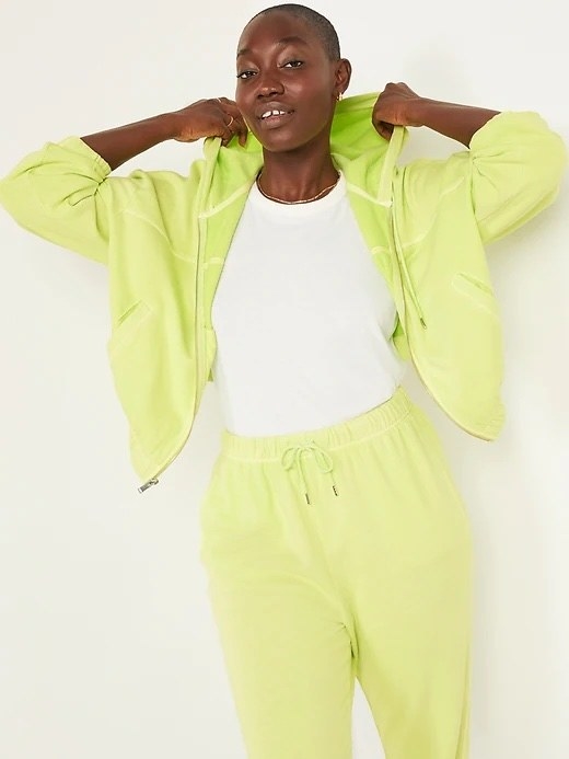 A person wearing a matching sweat suit as they lean against a plain wall