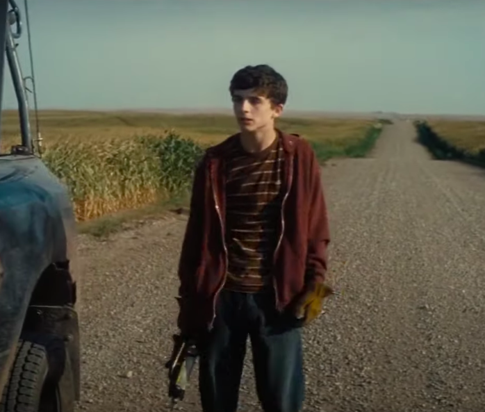 Timothée Chalamet standing next to a car on a dirt road.