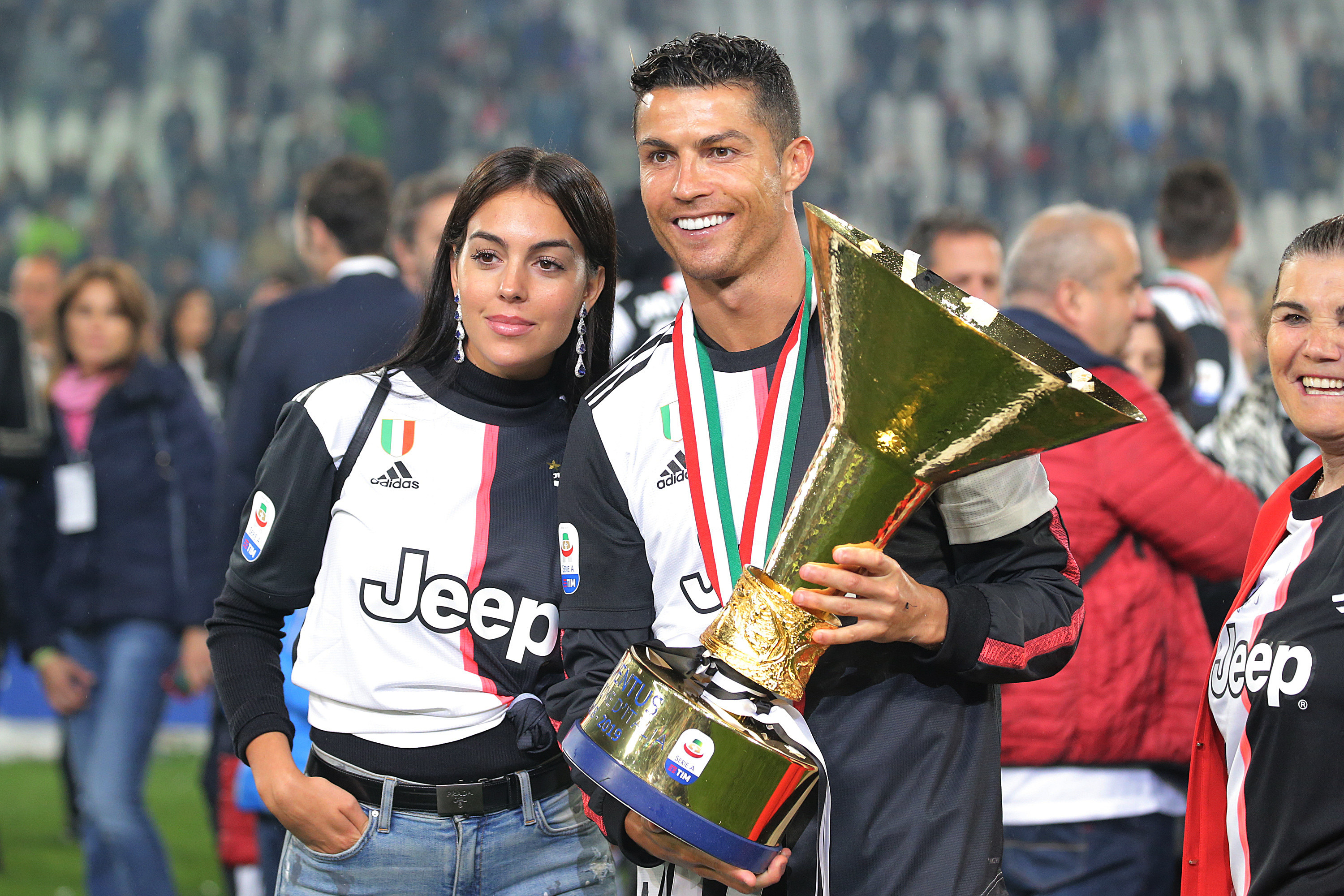 Georgina and Cristiano smiling on a soccer field while he holds a large trophy