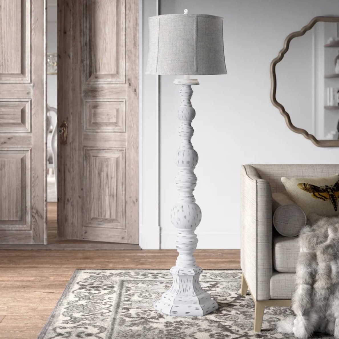 A traditional white floor lamp and lamp shade on a rug next to a couch