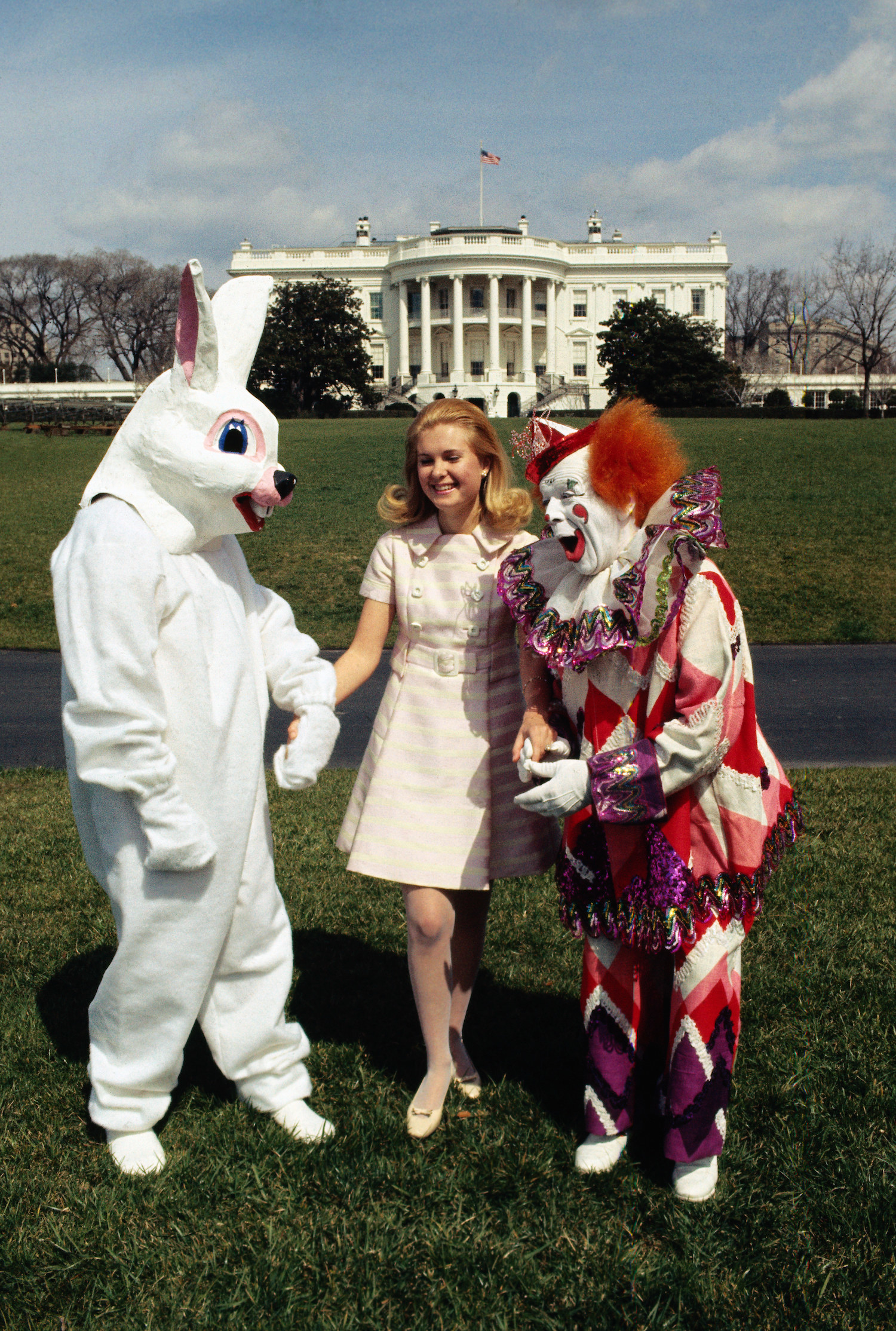 Tricia Nixon stands on grass in front of the White House with a terrifying clown and a very disturbing rabbit costume