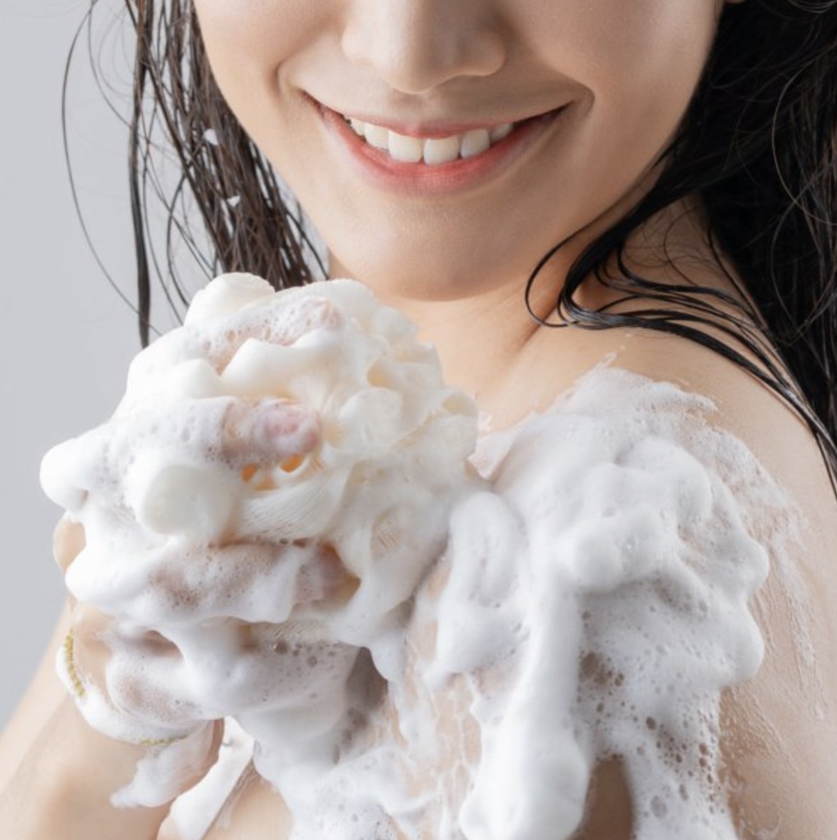 A person lathering their skin with body wash and a bath sponge