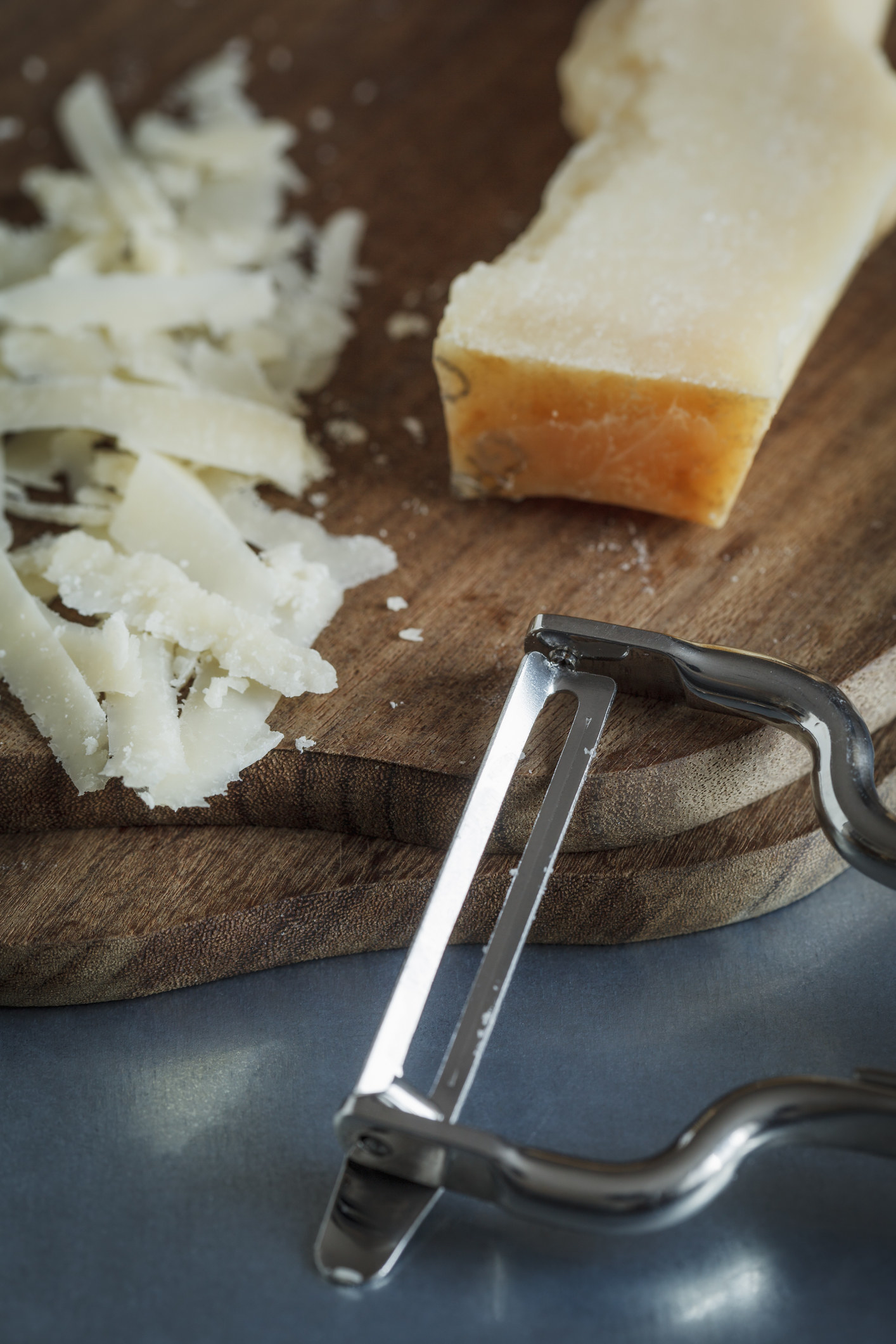 Shredded parmesan with peeler on chopping board.
