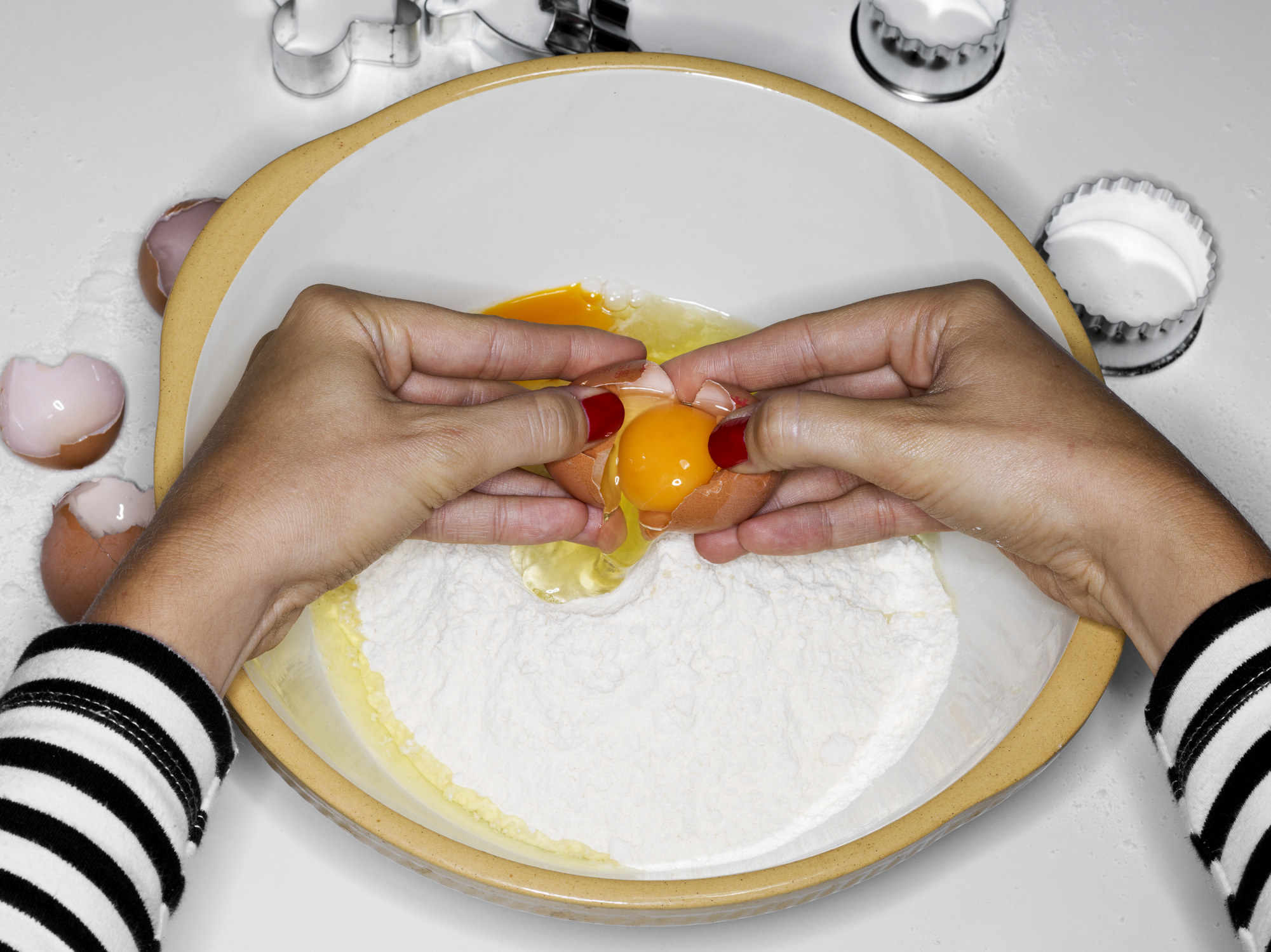 Feamle cracking egg into bowl with flour.