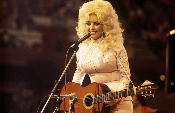 Dolly Parton holding a guitar and performing onstage.