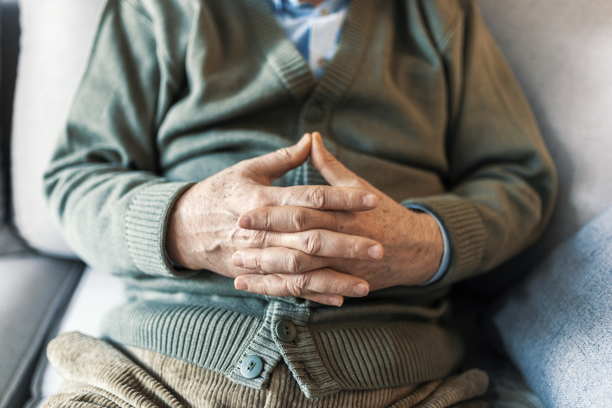 An older man sitting with his fingers linked.