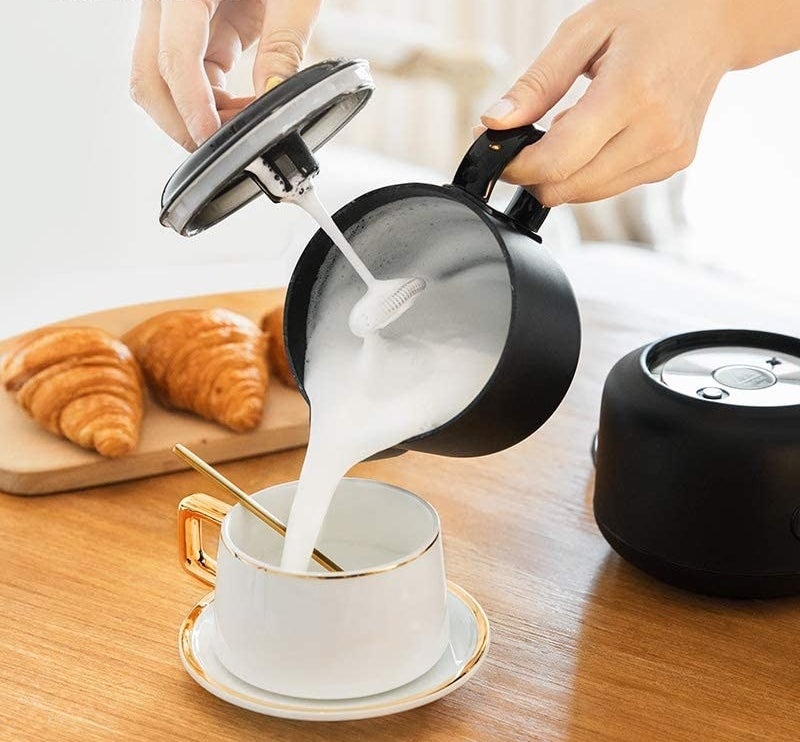 a person pouring milk foam out of the frother and into a teacup