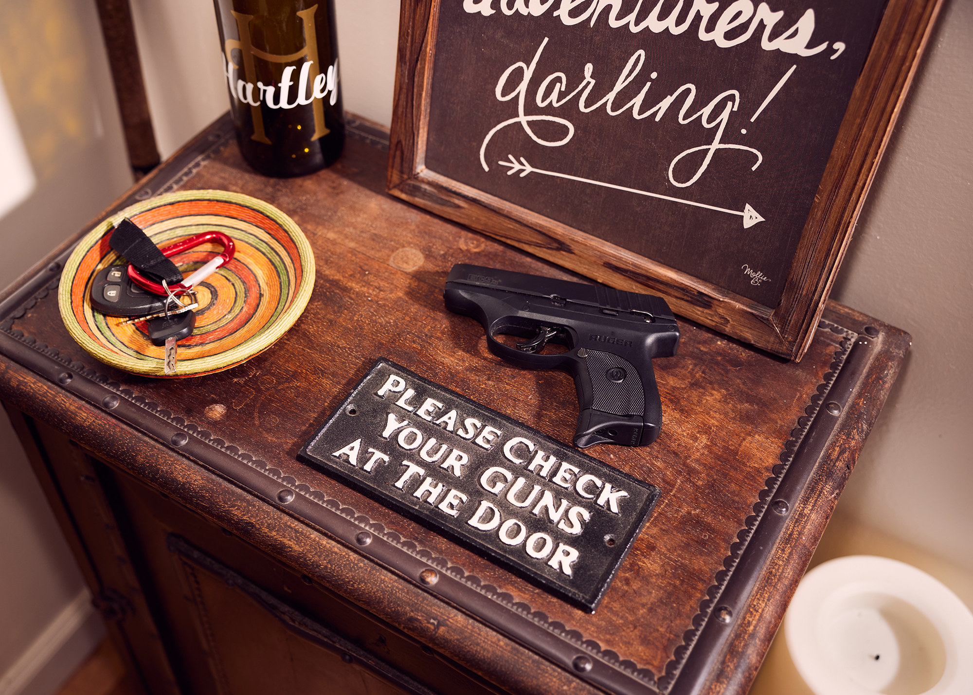 A sign that says Please Check Your Guns At The Door with a handgun next to it
