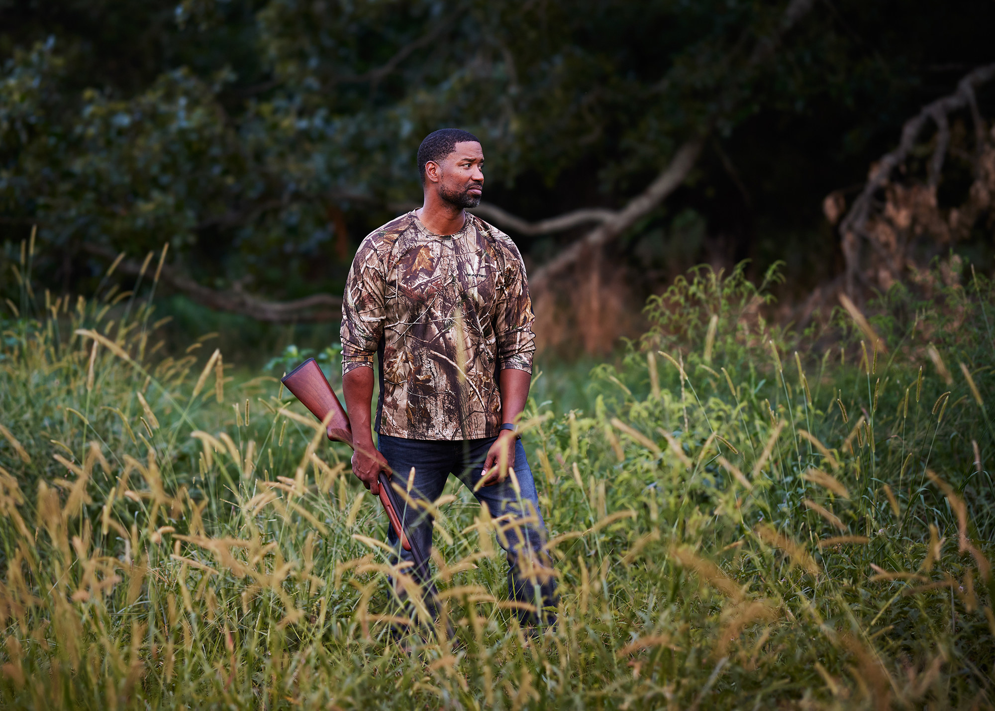 A man in camo holding a shotfun in a field