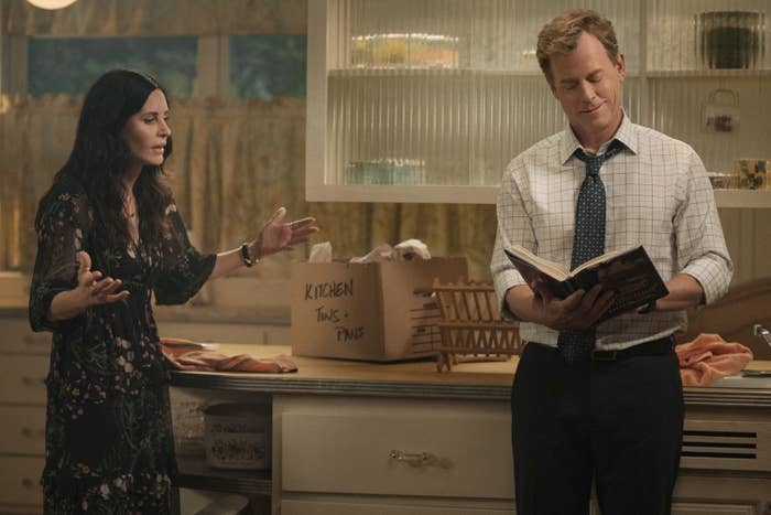 Greg Kinnear reads a book in kitchen while Courteney Cox speaks to him