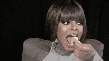 Janet Jackson putting food in her mouth and shaking her shoulders.