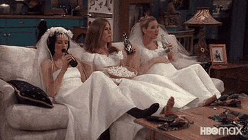 the characters drinking beers and eating popcorn on the couch while wearing wedding dresses