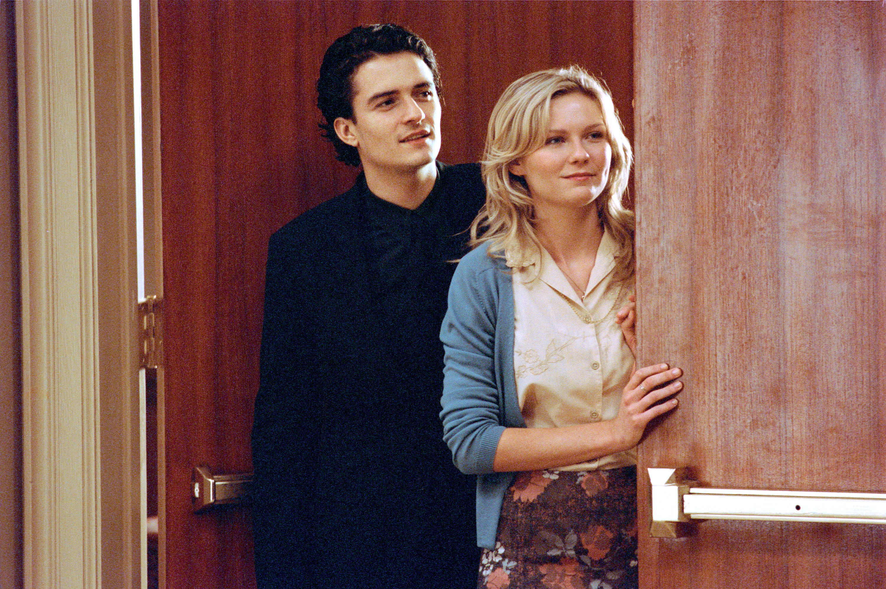Orlando Bloom and Kirsten Dunst stand behind a door smiling