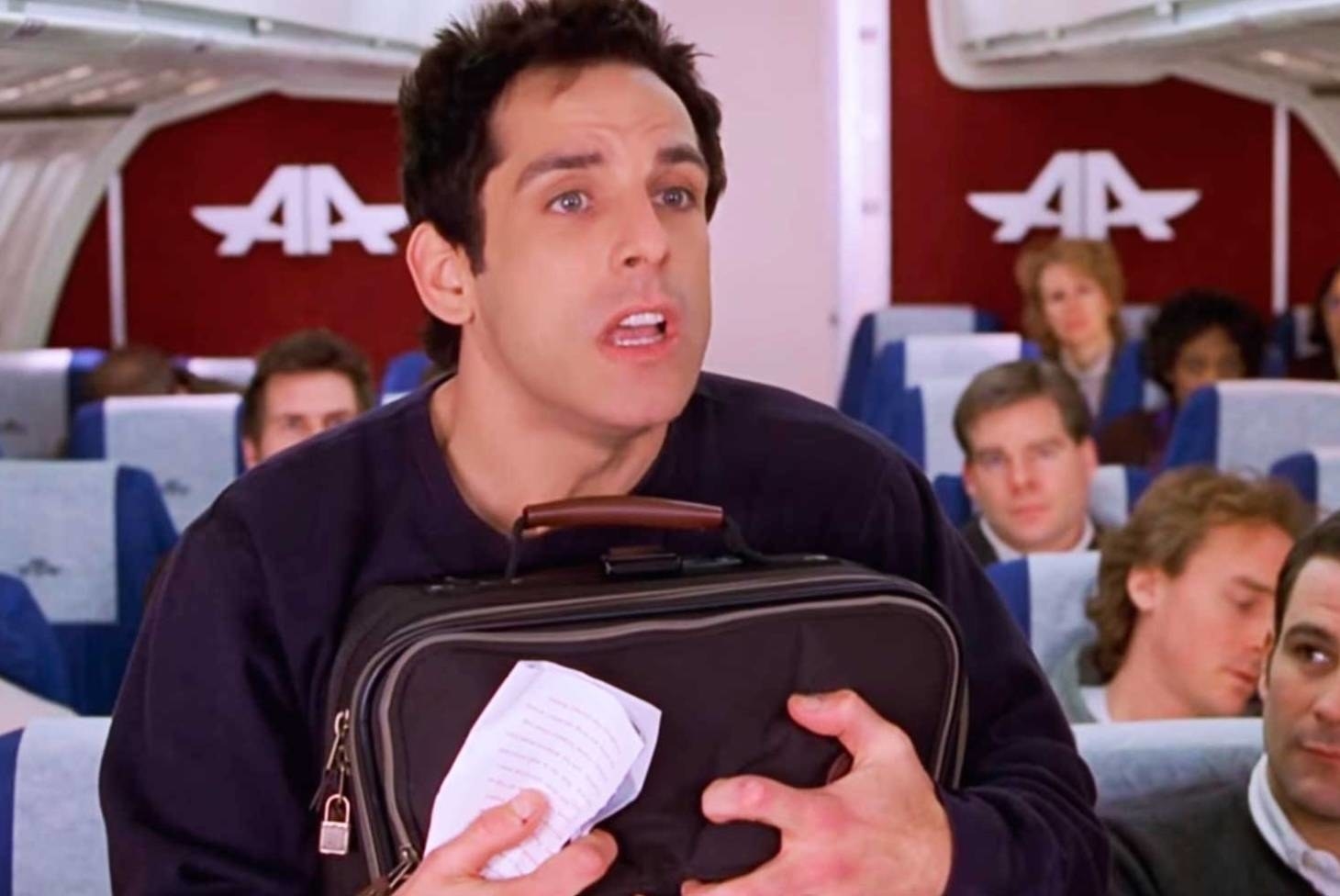 Ben Stiller stands on a plane holding his suitcase to his chest