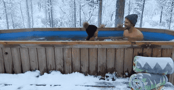 A man and a woman relaxing in a hot tub during a snowy day