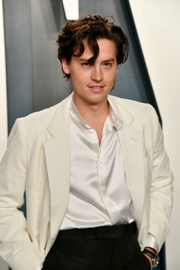 Cole Sprouse smiling with his hands in his pockets