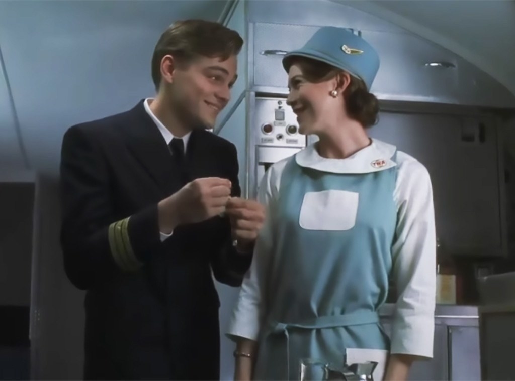 Leonardo DiCaprio and Ellen Pompeo smile at each other on a plane; he wears a pilot uniform and she wears a flight attendant uniform