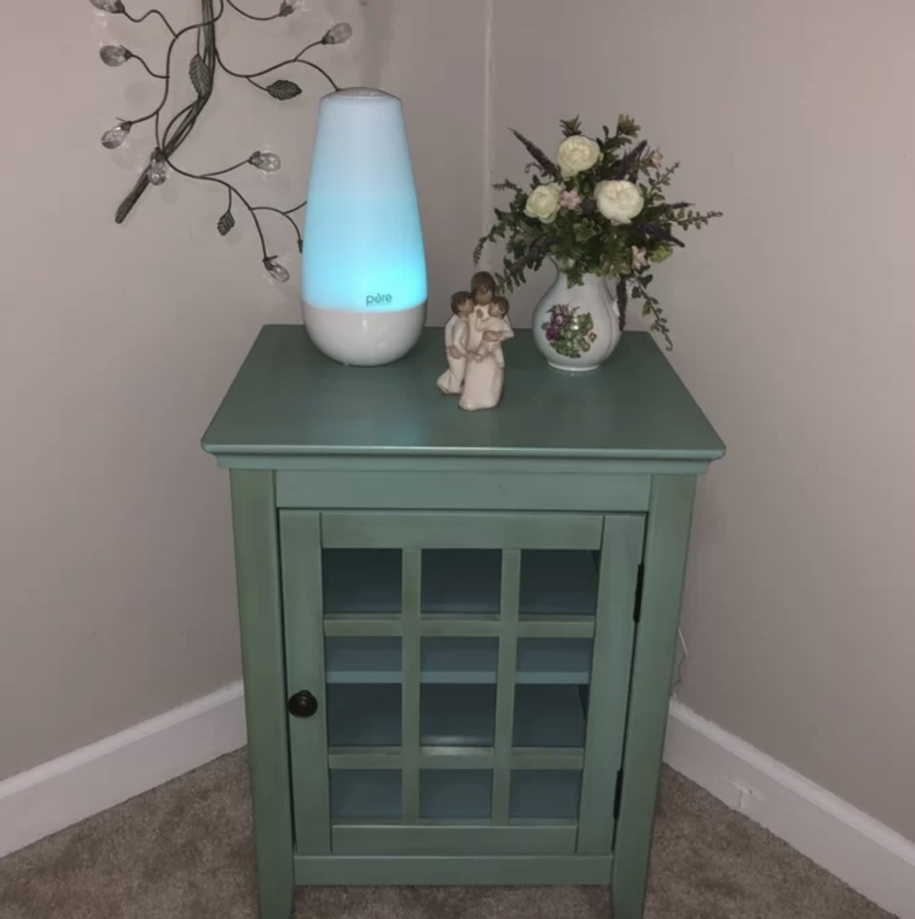 The blue humidifier is on top of a small green table with decor