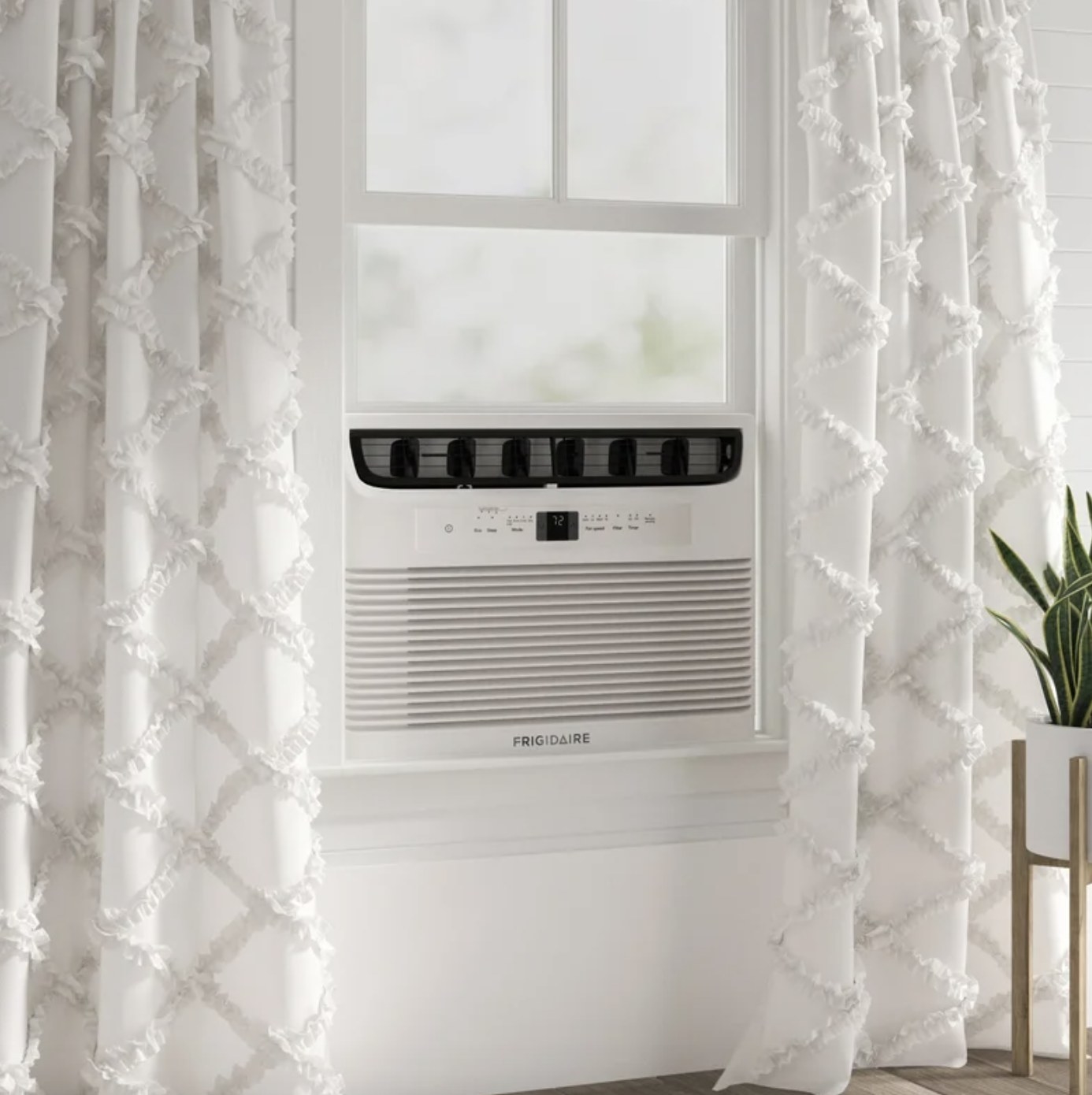 The white AC unit says &quot;FRIGIDAIRE&quot; and is in a window between two white curtains