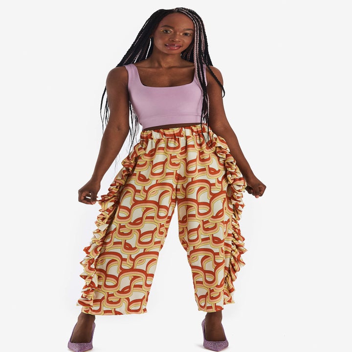 Model wearing funky printed pants, a purple crop top, and purple heels