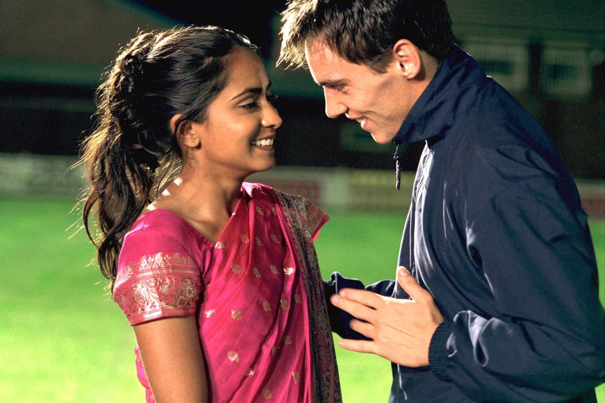 Jess wearing an Indian sari while talking to Coach Joe on a football field
