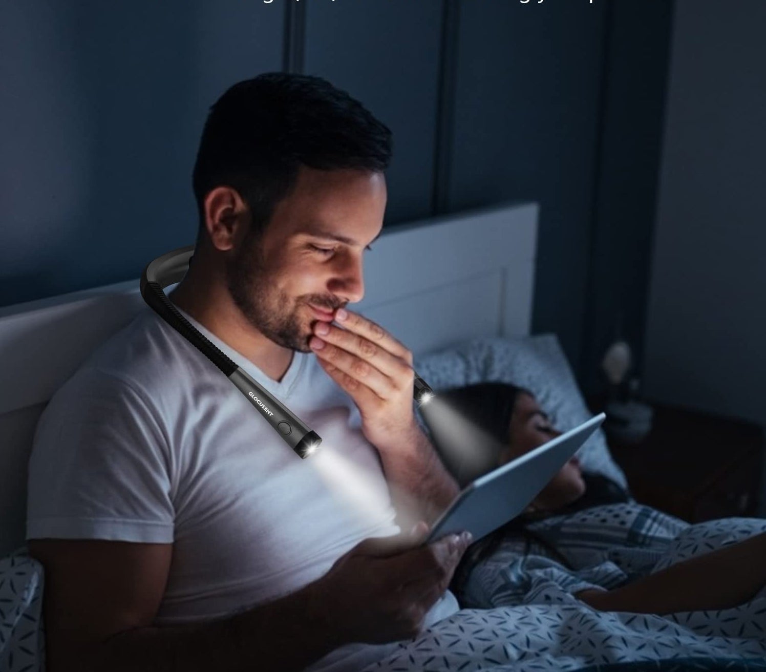 A person sitting up in bed with the book light wrapped around their neck