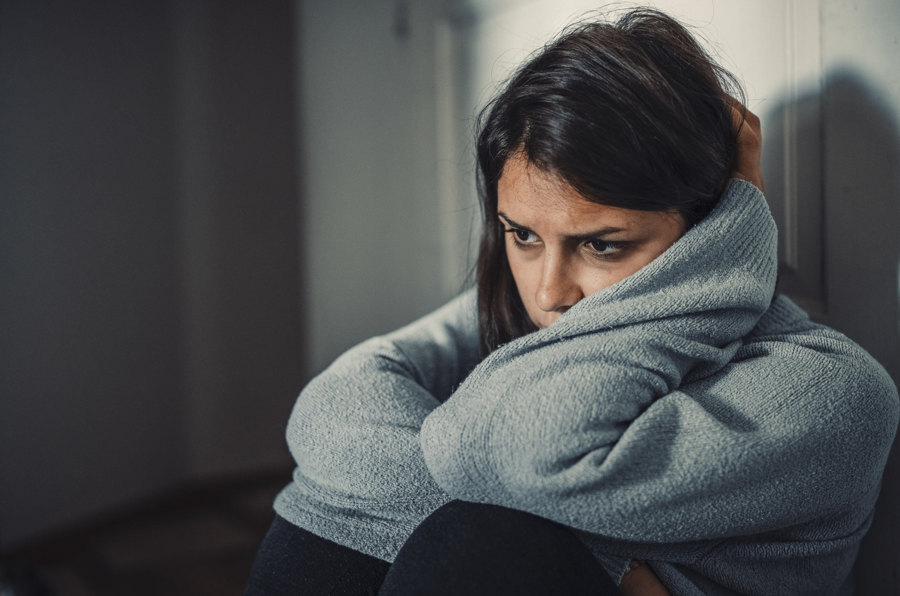 A woman sitting down looking sad with a sweater on