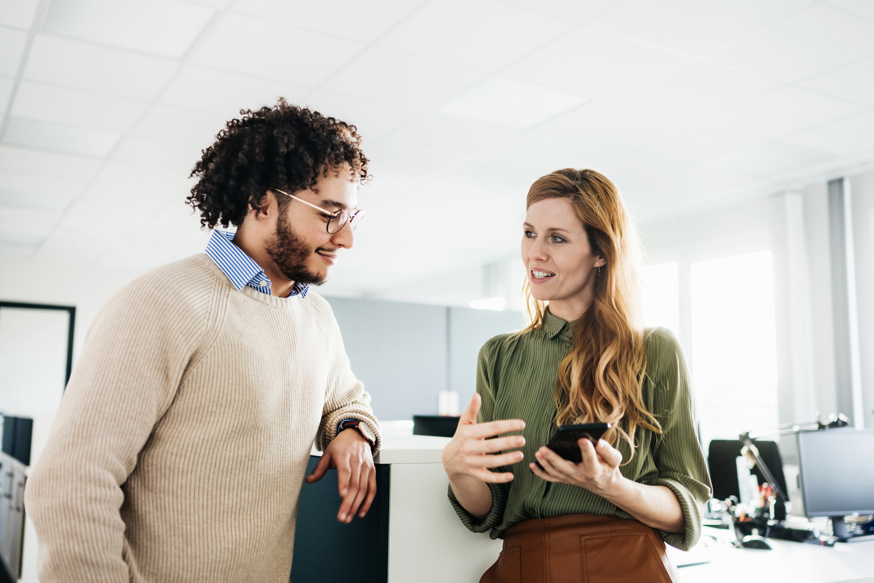 A woman talking to a co-worker while holding a phone