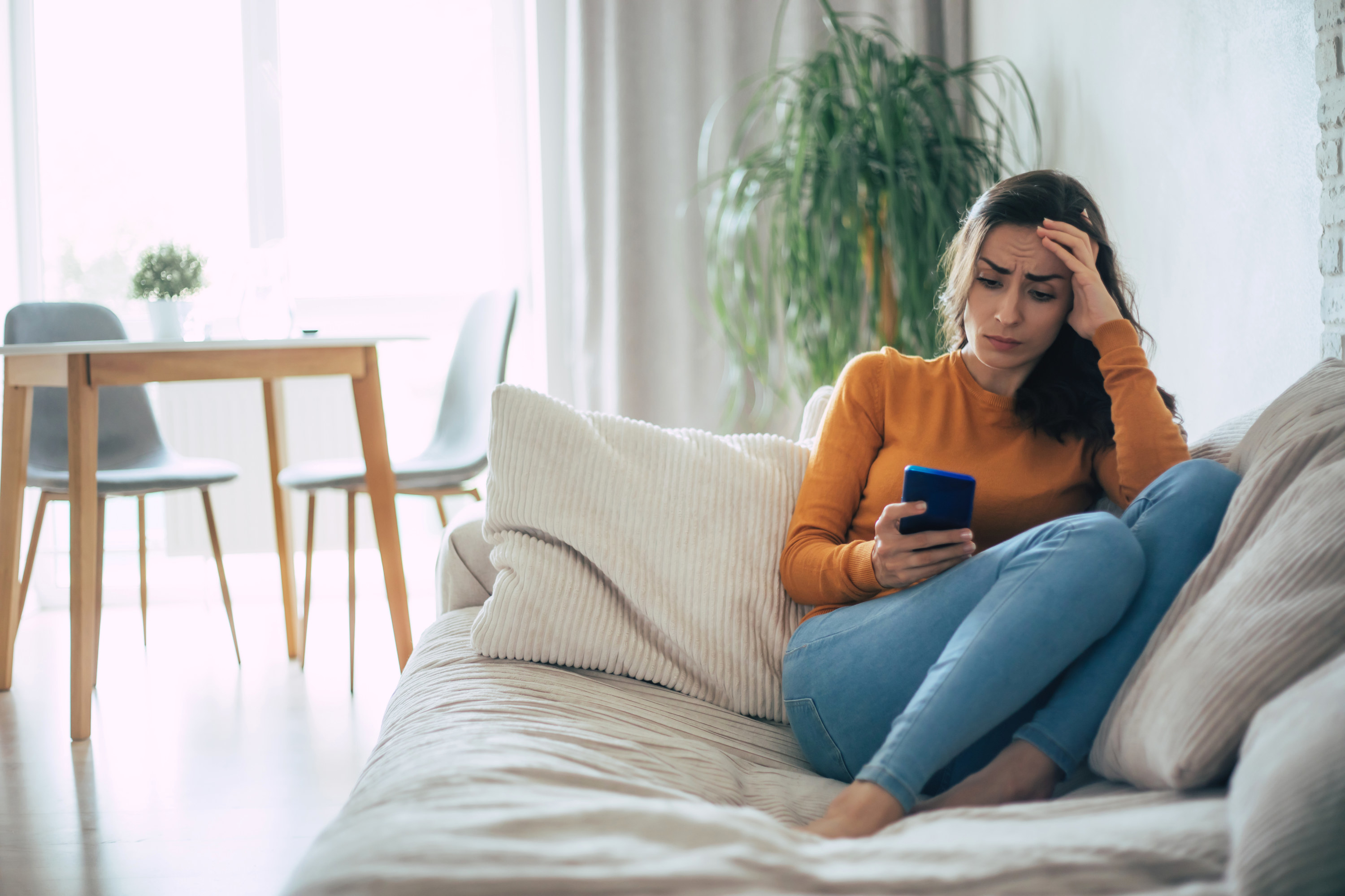 A woman looking worried while she&#x27;s on her phone at home