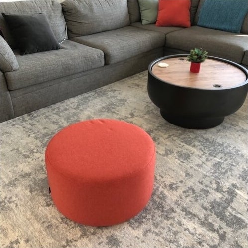 a reviewer photo of the coral ottoman on a gray rug