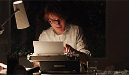 A bespectacled man typing on his typewriter