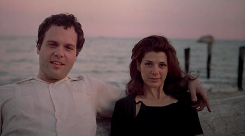 A man and a woman sit facing the camera with the sea in the background