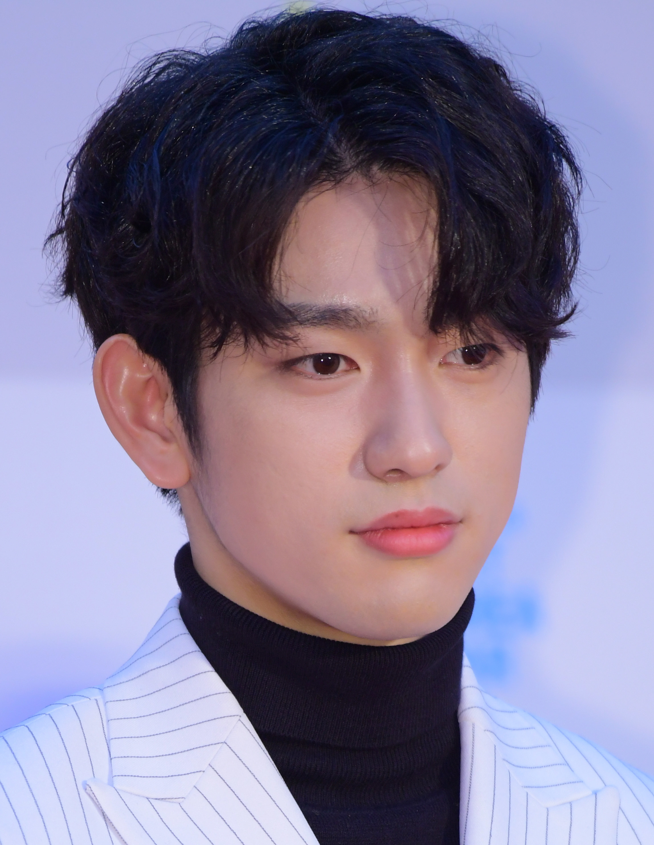 Head and shoulders portrait of Jinyoung, with wavy center-parted bangs and a turtle neck with a striped blazer over it