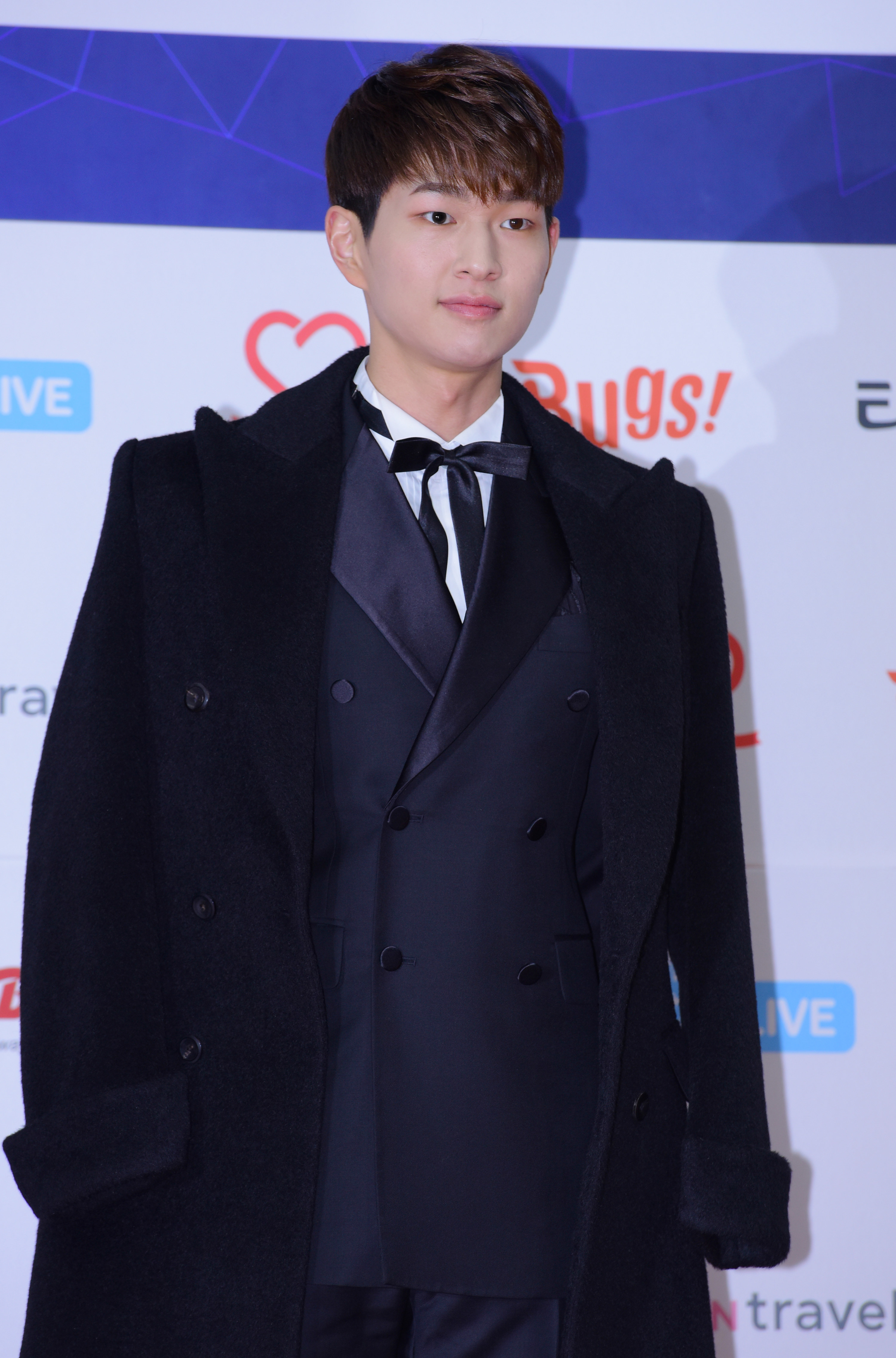 Onew in a smart suit with a coat over it, looking to be at a red carpet event