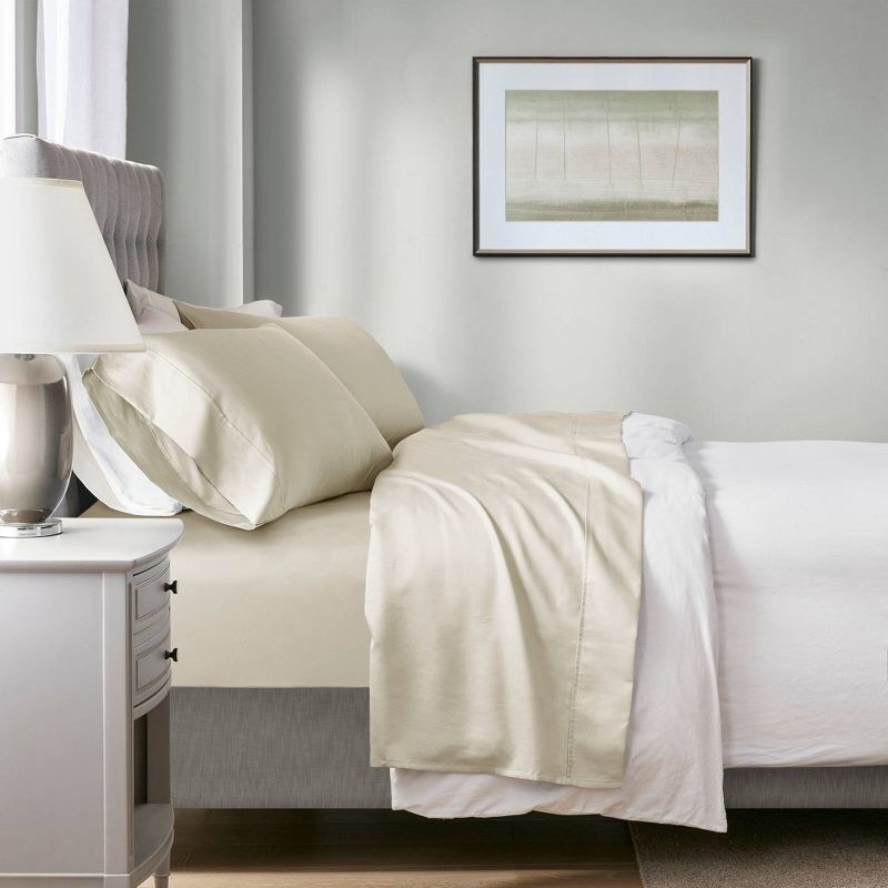 a made bed with cream sheets in a staged bedroom with a bedside table and art on the wall