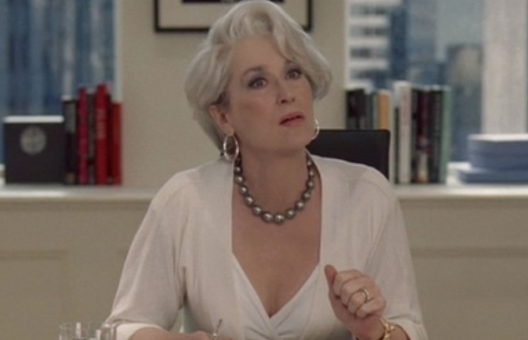 Miranda Priestly sits at her massive desk while wearing a long sleeve blouse