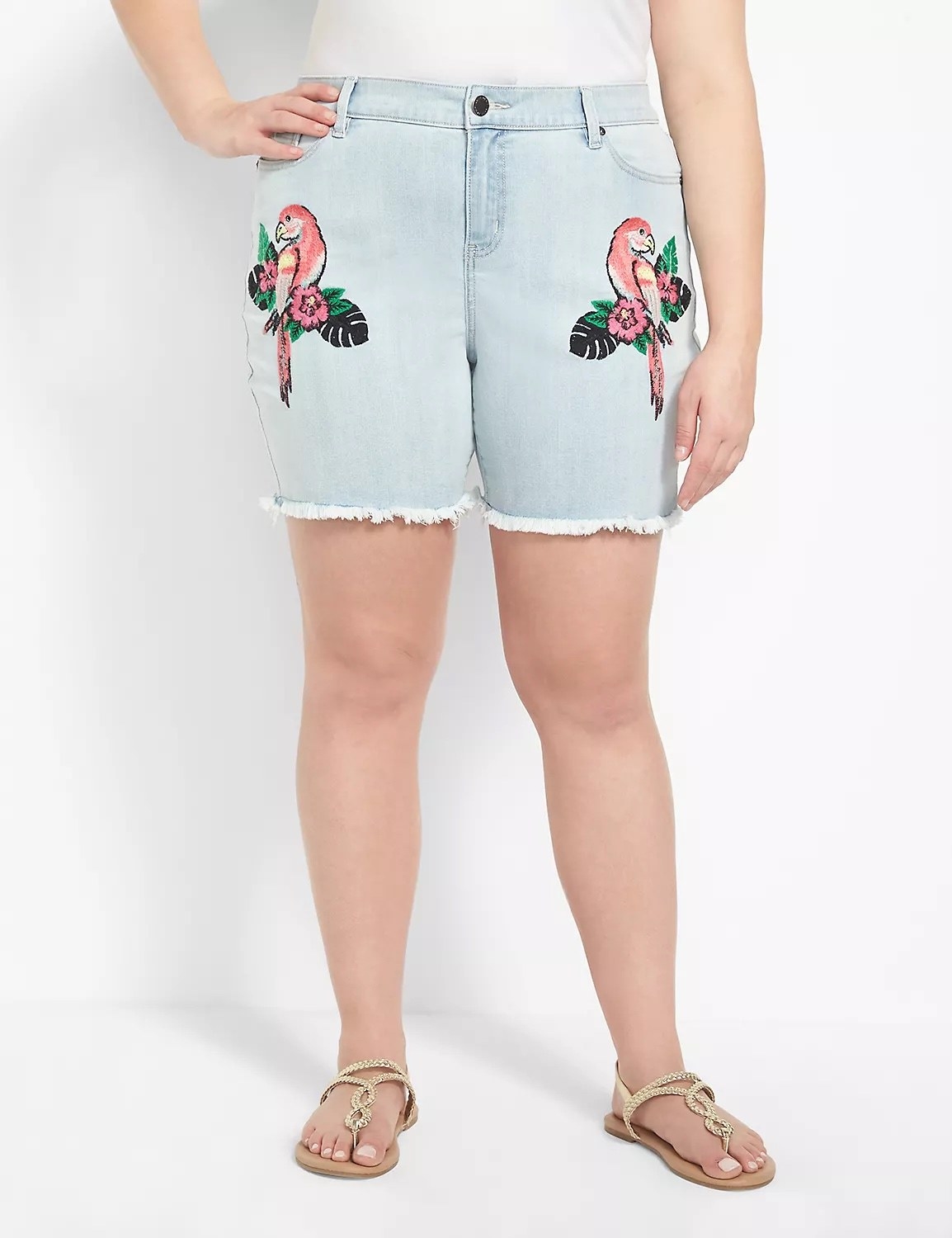 Model wearing light denim shorts with green and pink parrots and gold sandals