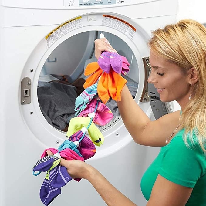 A person holding up the doodad with all of the socks on it in front of their washing machine