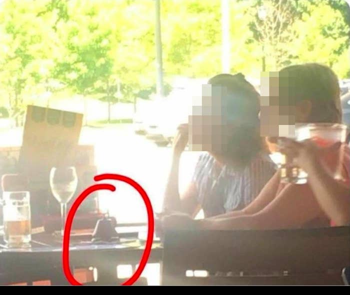 Two people with their faces obscured sitting at a table with some drinks on it and a circled bell