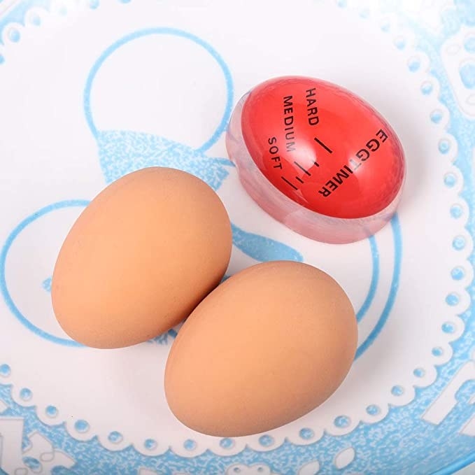 Two boiled eggs on a plate next to the egg timer