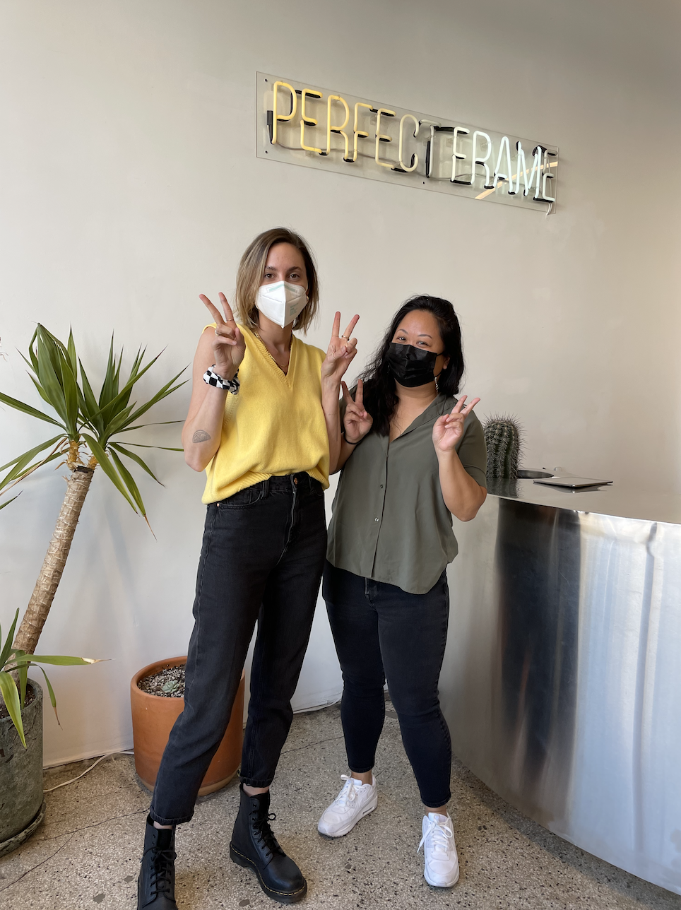 Crystal and Lara standing and posing in front of the &quot;Perfect Frame&quot; sign in the studio before their appointment