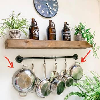 Reviewer image of silver pots hanging from black wall mounted bar and black S hooks underneath wooden shelf with plants and decorative tan bottles