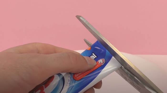 scissors cutting open a tube of toothpaste