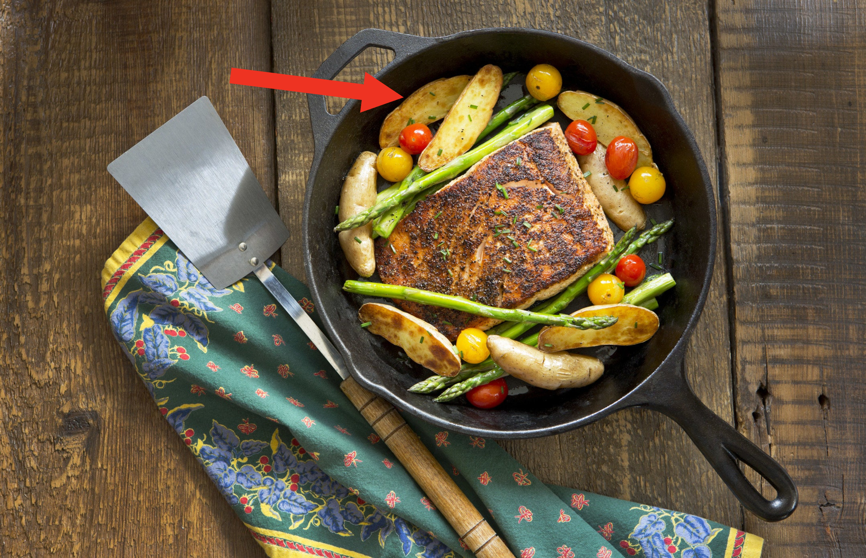 An arrow pointing to correctly cut fingerling potatoes in a pan with cherry tomatoes and salmon