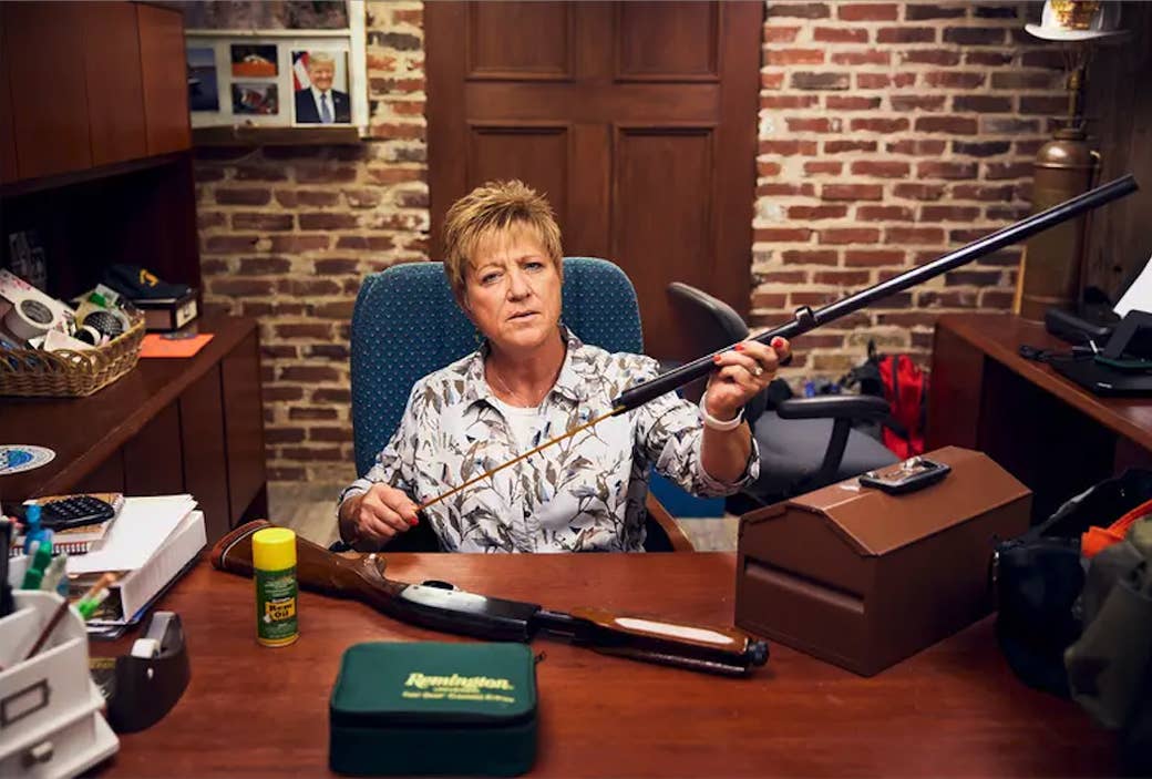 A woman sits behind a desk and cleans her gun