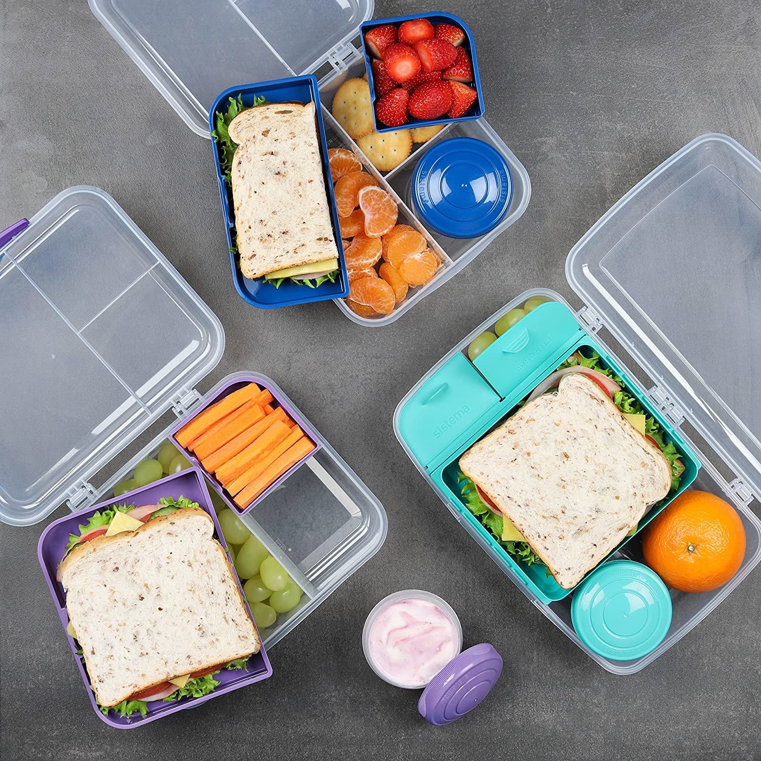 Three bento box food containers with sandwiches and fruit inside