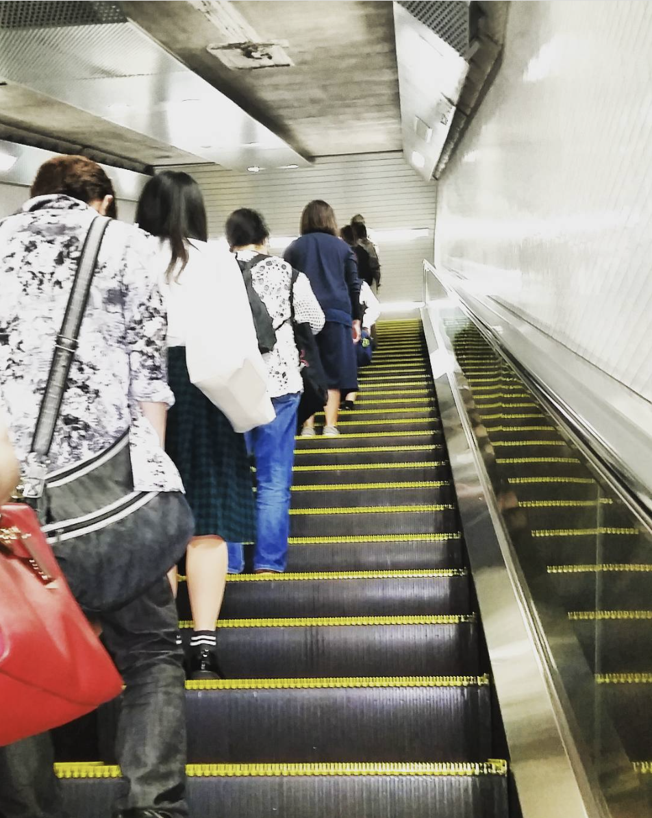 People standing to the left side of an escalator