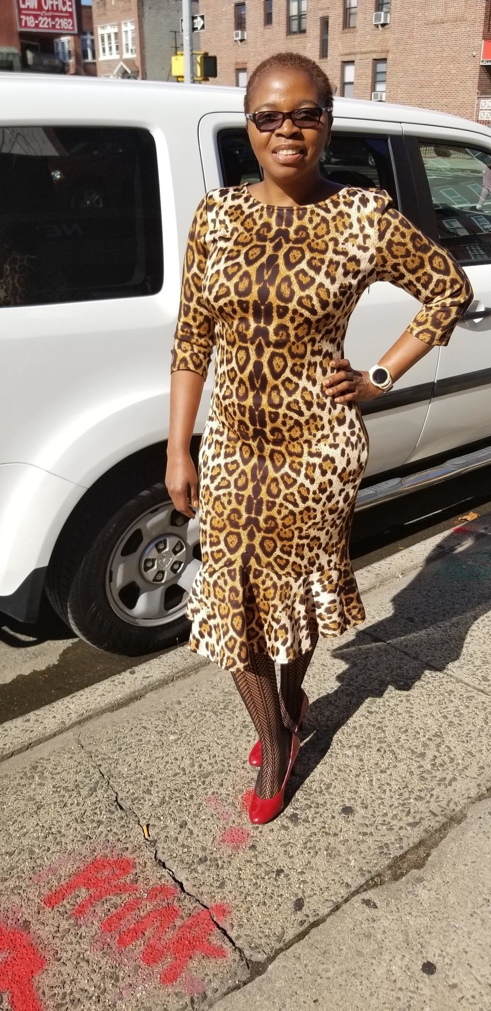 a customer review photo of them wearing a leopard print fit and flare dress standing in front of a white car